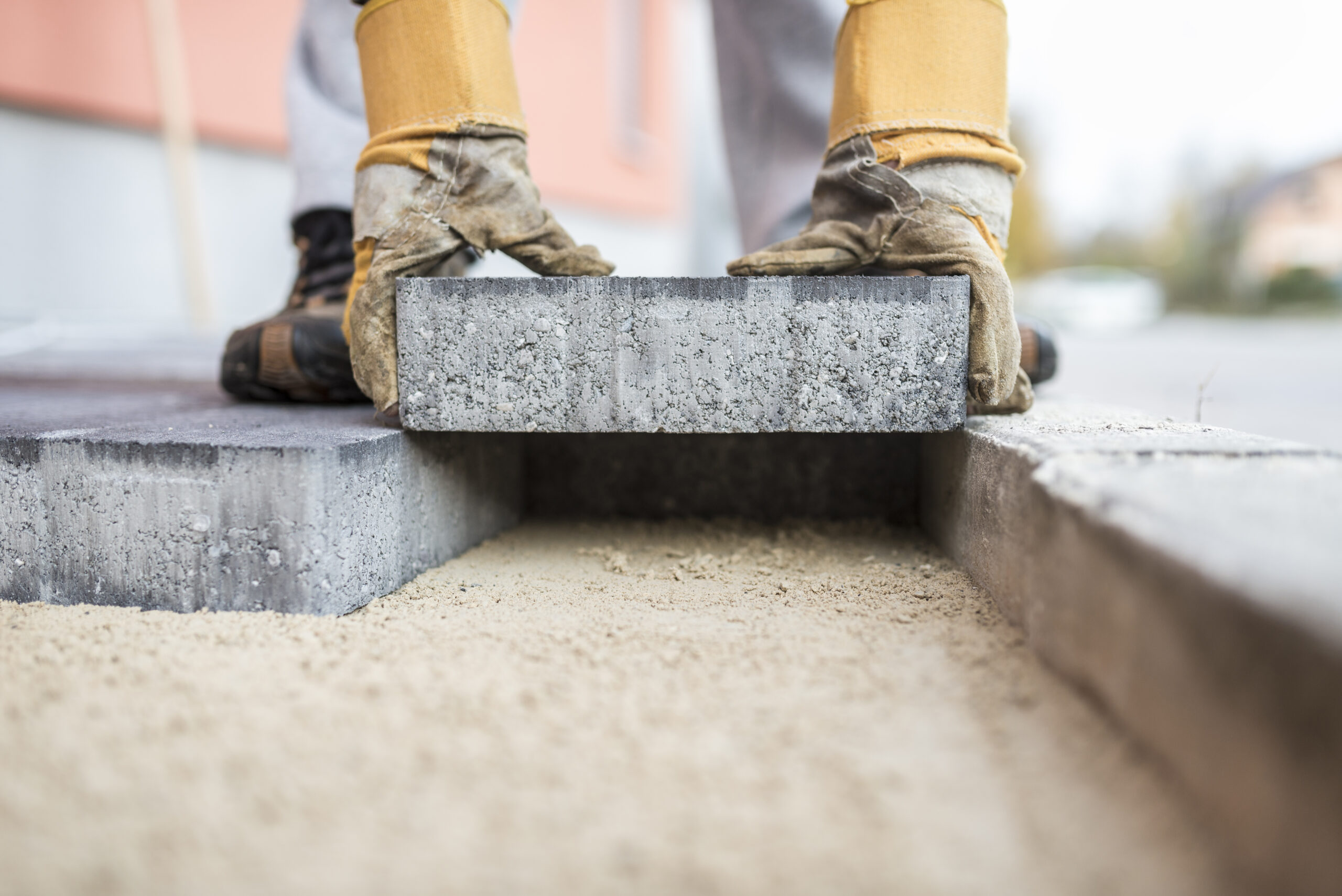 Close up of the gloved hands of a builder laying outdoor paving slabs on a prepared base.